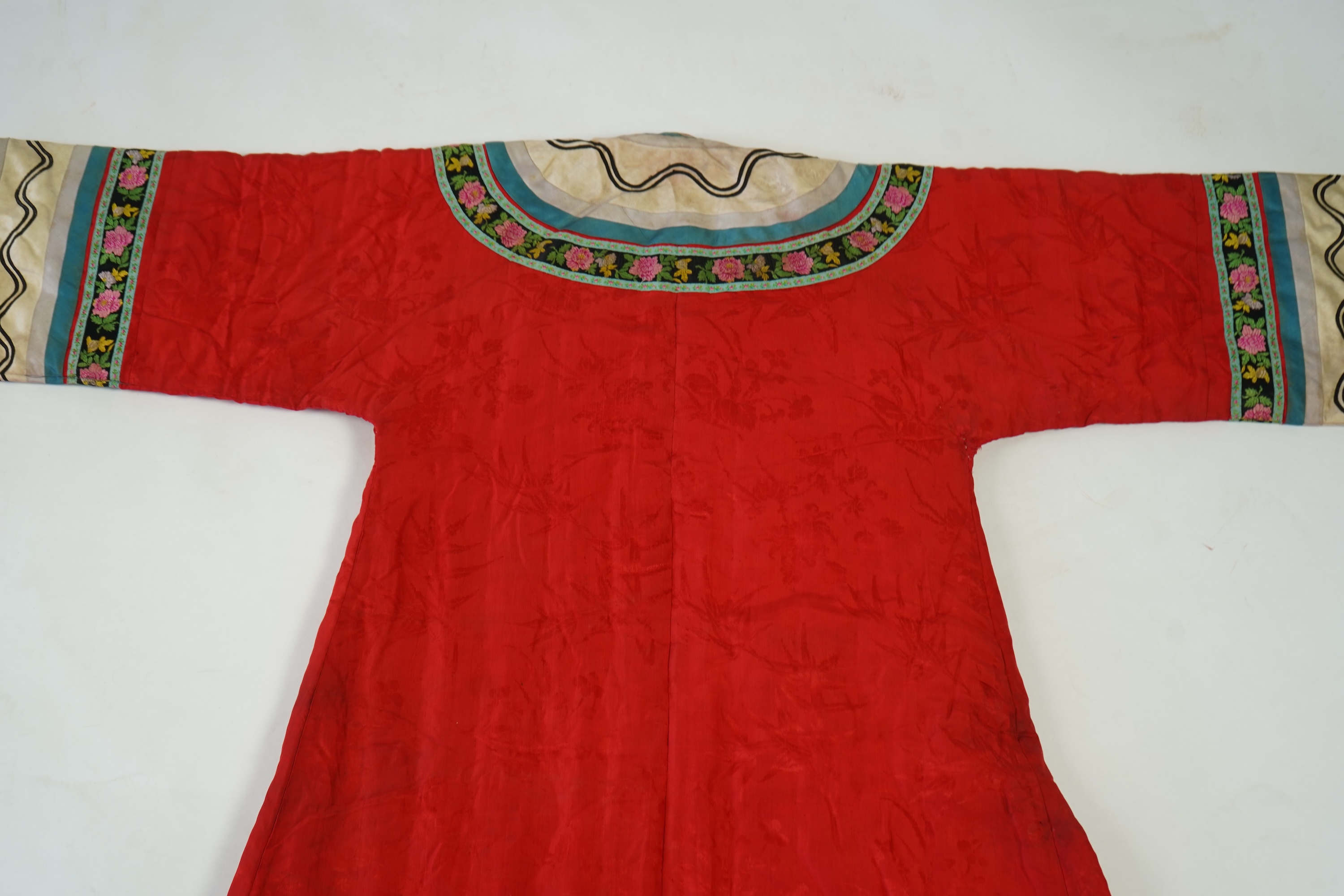 A late 19th century early 20th century Chinese red silk damask quilted Mandarin robe. Decorated with colourful rows braiding and ornate toggling. 116cm long. Condition - minor marks in places, may benefit from specialist